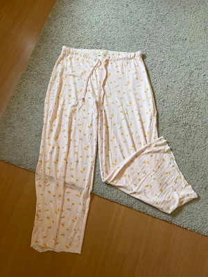 Ljusrosa pyjamasbyxor med citronmönster - Supersköna ljusrosa pyjamasbyxor med gulligt citronmönster och justerbar midja med dragsko. Byxorna är raka i modellen och har en avslappnad passform, perfekta för mysiga hemmakvällar. Materialet känns mjukt och svalt mot huden. OBS: avklippta så skulle säga att de passar i läng om du är vid 160-165cm lång 