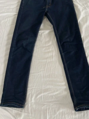 Mörkblå raka jeans - Säljer ett par mörkblå jeans med rak passform och klassiska kontrastsömmar. Jeansen har fem fickor och är tillverkade i ett slitstarkt denimtyg. Perfekta för en clean och enkel look.