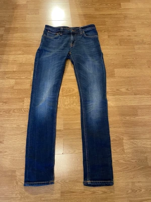 Mörkblå Nudie Jeans  - Snygga mörkblå slim fit jeans med klassisk femficksdesign och kontrastsömmar. Jeansen har en lätt tvättad look med slitningar på låren och knäna. Perfekta för en avslappnad och trendig stil.