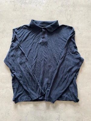 Mörkblå långärmad pikétröja - L - Snygg mörkblå långärmad pikétröja med klassisk krage och tre knappar framtill. Tillverkad i mjukt och tunt material som känns skönt mot huden. Perfekt för dig som gillar en enkel men stilren look.