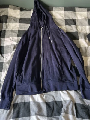 Mörkblå zip hoodie med kaninlogga - Snygg mörkblå hoodie med dragkedja från Playboy. Klassisk huva med dragsko och liten vit kaninlogga broderad på bröstet. Tillverkad i mjuk bomull, perfekt för en avslappnad streetwear-look.
