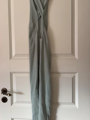 Mintgrön långklänning  - Snygg ribbad långklänning i mintgrön.  Klänningen har smala axelband som korsas i ryggen och en figurnära passform. Perfekt för sommarens varma dagar och har en stilren, minimalistisk look.