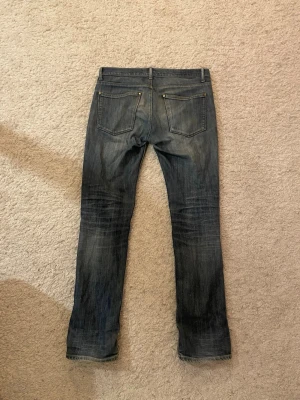 Acne studios jeans - Säljer ett par blå skinny jeans från Acne med slitningar och hål på knäna. Jeansen har klassisk femficksdesign, dragkedjegylf och en snygg tvättad look. Perfekta för en avslappnad och trendig stil. Det finns ett litet hål vid skrevet, men syns inte. Priset är inte hugget i sten.  30/32