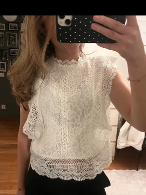 Vit spetsblus med volangdetaljer - Säljer en superfin vit blus i spets med volangdetaljer längs ärmar och nederkant. Använd ett fåtal gånger endast pga lite stor för mig. 