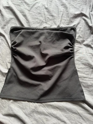 Svart tubtopp i stretchigt tyg - Säljer en svart tubtopp i stretchigt material. Toppen är enkel och stilren med lätt rynkade sidor för en snygg passform. Perfekt att matcha med jeans eller kjol för en trendig look.
