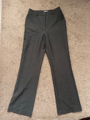 Gråa kostymbyxor med ränder Bubbleroom - Snygga grå kostymbyxor från Bubbleroom med vita tunna kritstrecksränder. Byxorna har raka ben, hällor för skärp och klassisk kostymlook. Perfekta för en stilren och trendig outfit. Använda  endast en gång💗