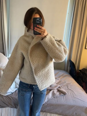 Beige teddyjacka med bred krage - Mysig och trendig teddyjacka i beige med bred krage och avslappnad passform. Jackan är gjord i fluffigt teddy-material och har långa ärmar. Perfekt för att hålla sig varm och se stylish ut under kyliga dagar.