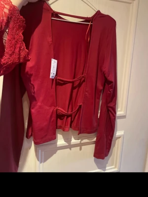 Röd långärmad topp med snörning - Cool röd långärmad topp med snörning framtill och öppen detalj. Materialet är mjukt och stretchigt, perfekt för att skapa en edgy look. Rund halsringning och croppad passform som ger en modern vibe.