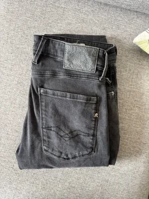 Svarta jeans från Replay - Snygga svarta jeans från Replay med klassisk femficksmodell och diskret logga på bakfickan. Jeansen har raka ben och är tillverkade i ett mjukt denimtyg som ger en skön passform. Perfekta för dig som gillar en stilren och tidlös look.