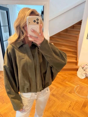 Olivgrön oversized mockaskjorta - Snygg olivgrön skjorta i mocka med oversized passform och klassisk krage. Skjortan har långa ärmar och stilrena sömdetaljer framtill. Perfekt för dig som gillar en avslappnad och trendig look.