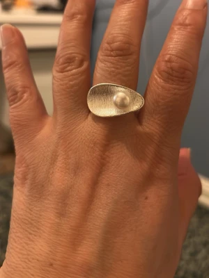 Bianca ring med pärldetalj - Snygg silver  ring  med en unik, organisk formad skål och en vit pärldetalj i mitten. Ringen har en borstad yta som ger en modern och stilren känsla. Perfekt för dig som gillar statement-smycken och vill sticka ut lite extra.