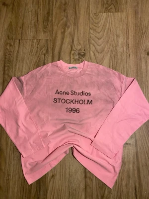 Rosa långärmad topp Acne Studios - Cool rosa långärmad topp från Acne Studios med tryck 'STOCKHOLM 1996' på bröstet. Oversized fit och rund halsringning. Perfekt för dig som gillar streetstyle och vill sticka ut med en färgglad look.