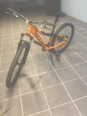 Orange mountainbike från Rockrider - Säljer en orange mountainbike från Rockrider med svart sadel och svarta detaljer. Cykeln har grova däck, skivbromsar och sportig ramdesign. Perfekt för dig som gillar att cykla i terräng eller på grusvägar. Pedaler och handtag i svart plast. Kostar 4999 sek direkt från stadium