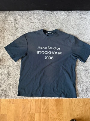Mörkblå Acne Studios t-shirt - Cool svart t-shirt från Acne Studios med tryck 'STOCKHOLM 1996' på bröstet. Klassisk passform med rund hals och korta ärmar. Perfekt för dig som gillar stilrena och trendiga plagg med streetkänsla. Helt ny!