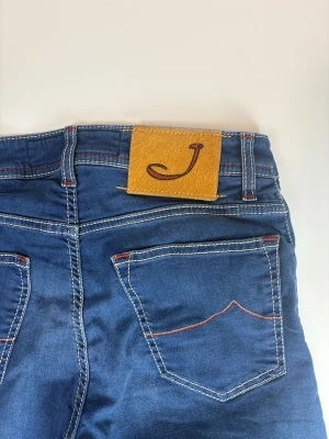 Blå jeans från Jacob Cohen - Snygga blå jeans från Jacob Cohen med klassisk femficksdesign, kontrastsömmar i vitt och rött samt en gul patch med J-logga bak. Jeansen har rak passform och är tillverkade i mjuk denim med stretch för extra komfort.