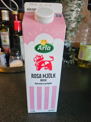 Arla rosa mjölkdryck jordgubb - En 1-liters tom förpackning Arla rosa mjölkdryck med smak av jordgubb. Kartongen är vit och rosa med en tecknad rosa ko på framsidan. 