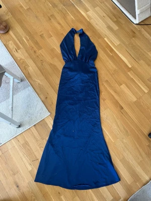 Marinblå långklänning med halterneck - Snygg marinblå långklänning med halterneck och djup urringning framtill. Klänningen har en elegant, figurnära passform och är tillverkad i ett glansigt material som ger en lyxig känsla. Perfekt för speciella tillfällen när du vill sticka ut. OBS! Kan gå ner lite pris vid seriöst intresse:)