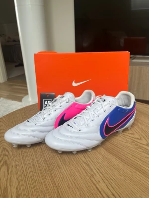 Nike fotbollsskor vit/blå/rosa - Säljer nu mina fotbollskor som är använda endast 1 träning. Köpte dom o använde dom, därefter kände jag att dom inte passa. Så jag kunde inte lämna tillbaka dom. Dom är som nya och allt följer med.