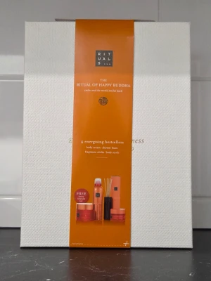 Rituals The Ritual of Happy Buddha kit - Säljer ett exklusivt presentkit från Rituals, The Ritual of Happy Buddha. Innehåller body cream, shower foam, doftstickor och body scrub. Produkterna har en energigivande doft och kommer i orange och vita förpackningar med stilren design.