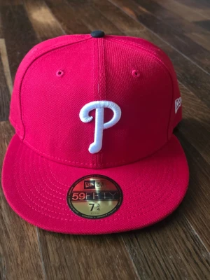 Röd New Era 59FIFTY keps - Säljer en röd New Era 59FIFTY keps från MLB Authentic Collection. Kepsen har en klassisk form med böjd skärm och är tillverkad i slitstarkt material. Perfekt för dig som gillar sportiga accessoarer och vill ha en officiell on-field cap.