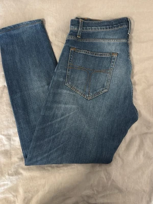 Blå raka jeans med klassisk tvätt - Säljer ett par blå jeans med rak passform och klassisk femficksdesign. Jeansen har en snygg tvätt med lätt slitning och kontrastsömmar. Perfekta till en avslappnad stil och passar till det mesta. Materialet är mjukt denim i bomull.30/31