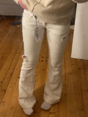 Vita bootcut jeans med slitningar - Snygga vita bootcut jeans med slitningar. De är i tall och innerbenslängden är 90cm. Endast använda 3gånger!