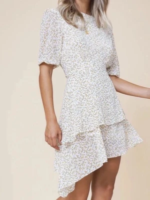 Blommig kortklänning med puffärm - Supersöt kortklänning i ljusgul med små gula blommor och diskreta gröna detaljer. Klänningen har puffiga trekvartsärmar och en lätt utsvängd kjo som är asymmetrisk . Perfekt för sommarens alla tillfällen! Materialet känns lätt och luftigt.