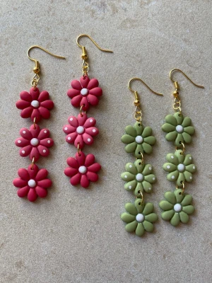 2 par handgjorda örhängen – blomdesign - 2 par handgjorda örhängen i polymerlera  Blomdesign i två färger – rosa och grönt.  Ca 8 cm långa – tydliga statementörhängen som ändå är lätta att bära.  Varje par är gjort för hand och kan variera något i detaljer. Sälja även separat i andra annonser.   Antiallergiska detaljer Lätta Skickas