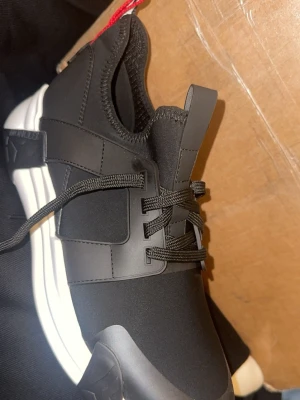 Svarta Moncler sneakers med vit sula - Snygga svarta sneakers från Moncler med vit chunky sula och svarta snören. Skorna har en elastisk ovandel och en röd, vit och blå Moncler-detalj baktill. Perfekta för dig som gillar stilrena och sportiga skor med premiumkänsla.