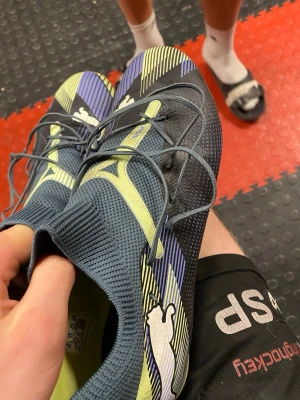 Puma future - Säljer ett par Puma Ultra fotbollsskor i blått och gult med vita detaljer. Skorna har snörning, stickad strumpliknande krage och mönstrad ovandel i syntetmaterial för bra grepp och känsla på planen. Perfekta för dig som vill ha lätta och snabba skor. Väldigt bra skick, endast lite smutsiga.