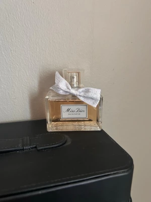 Miss Dior Eau de Parfum 100ml - Miss Dior Eau de Parfum från Dior i en elegant glasflaska med ljusrosa doft och en söt silverfärgad rosett runt halsen. Flaskan har en klassisk fyrkantig form och en transparent kork. Perfekt för dig som gillar lyxiga och feminina parfymer. Knappt använd 