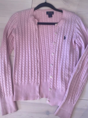 Ljusrosa kofta Polo Ralph Lauren - Ljusrosa kofta från Polo Ralph Lauren med rund halsringning och knäppning framtill.  Ska passa åldern 12-14, jag kan fortfarande ha den och när xxs-xs 