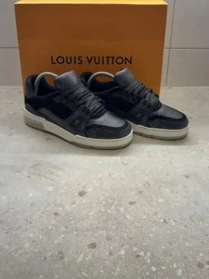 Louis Vuitton svarta sneakers - Stilrena svarta Louis Vuitton sneakers med lågt skaft. Skorna har en mix av läder och mocka, med diskreta LV-loggor på sidan och tungan.det finns även kvitto. .strolk 40,5 men passar 41,5