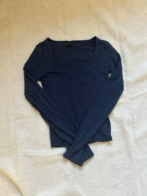 Mörkblå långärmad topp Gina Tricot - Mörkblå långärmad topp från Gina Tricot med rundad, djup urringning. Tillverkad i mjuk bomull och har en enkel, clean design som är lätt att styla till olika looks.