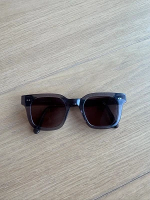  Solglasögon från Chimi - Stilrena svarta solglasögon med breda bågar och fyrkantig form. Glasen är mörka och bågarna är i blank plast, vilket ger en modern och cool vibe. Perfekta för att lyfta vilken outfit som helst. Använda ett par säsonger. Någon repa kan finnas i glaset, men inget som påverkat när jag använt dem. Skalmarna har justerats hos och kan säkert göras igen för att anpassa. 