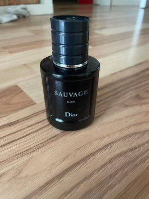 Dior Sauvage Elixir parfym - Dior Sauvage Elixir är en exklusiv parfym i en mörk, nästan svart glasflaska med silverdetaljer och tydlig logga. Flaskan har en rund form och en robust, stilren design som känns lyxig och modern. 