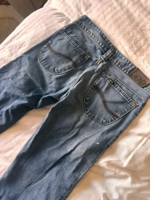 Blå bootcut jeans från Lee - Snygga blå bootcut jeans från Lee med klassiska bakfickor och ljusa slitningar. Jeansen har normalhög midja, bälteshällor och är tillverkade i denim med en skön känsla. Perfekta för en avslappnad och trendig look. Har dessvärre lite färgfläckar på sig, se sista bilderna 