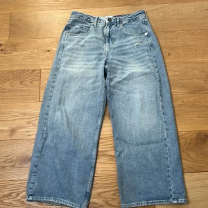 Ljusblå wide jeans från Urban outfiters BDG - Säljer ett par ljusblå jeans från BDG med breda ben och klassisk femficksdesign. Midian är 28 men mer som 30. Jeansen har en avslappnad passform, hög midja och snygga slitningar framtill. Bakfickan har en broderad BDG-logga. Perfekta för en chill och trendig look.