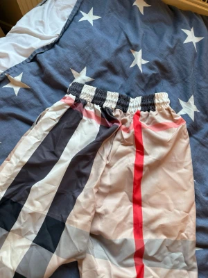 Burberry shorts  med snörning - Snygga shorts med breda ränder i svart, vitt, grått och rött. De har elastisk midja och snörning för extra passform. Perfekta för sommaren och har en avslappnad vibe. Materialet känns lätt och luftigt.