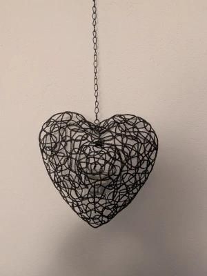 Hjärta i metalltråd med glaslykta - Dekorativt hjärta i svart metalltråd med inbyggd glaslykta för värmeljus. Hängs upp med kedja och passar perfekt som mysig inredningsdetalj. Ger ett stilrent och modernt intryck med sin öppna design.