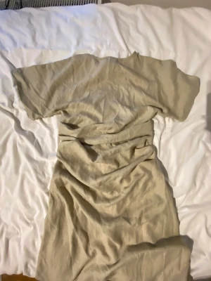 Beige långklänning i linne - En enkel och stilren beige långklänning i mjukt linnematerial. Klänningen har korta ärmar och rak passform, perfekt för varma dagar. Den neutrala färgen gör den lätt att matcha med accessoarer och skor.