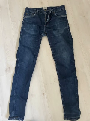 Mörkblå slim fit jeansEast West - East West Snygga mörkblå slim fit jeans med klassisk femficksdesign och lätt slitna detaljer. Jeansen har normal midja och smala ben, perfekta för en trendig och avslappnad look. Tillverkade i denim med stretch för extra komfort.  Lite lagade enligt bild    Storlek 30.32
