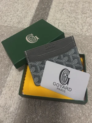 Goy4ard plånbok grå - Snygg korthållare i svart och grått med det klassiska mönstret. Tillverkad i läder och canvas, perfekt för kort och ID. Kommer med originalask och tygpåse. Stilren och lyxig accessoar för dig som gillar exklusiva detaljer.