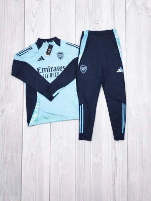 Arsenal träningsset från Adidas - Snyggt träningsset från Adidas med Arsenal-logga. Setet består av en ljusblå långärmad tröja med svarta detaljer och matchande mörkblå träningsbyxor med ljusblå ränder. Perfekt för fotboll eller gym. Materialet är lätt och andas bra.