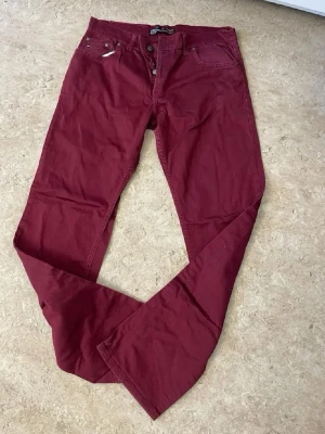 Mörkröda jeans med bootcut - Snygga mörkröda jeans från Replay med bootcut-modell och klassiska fem fickor. Jeansen har knappgylf och är tillverkade i ett mjukt bomullsmaterial. Perfekta för dig som vill sticka ut med färg och stil.