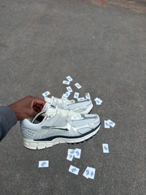 Nike silverfärgade sneakers - Snygga sneakers från Nike i silver och vitt med mesh och syntetmaterial. Skorna har en låg profil, klassisk swoosh på sidan och detaljer i metallic. Perfekta för dig som vill ha en modern och sportig look.