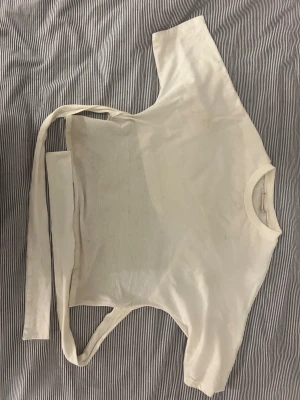 Vit croppad topp med knytband - Säljer en vit croppad topp med rund hals och trekvartsärm. Toppen har långa knytband i midjan som ger en snygg omlott-effekt. Perfekt att styla med höga jeans eller kjol för en trendig look.