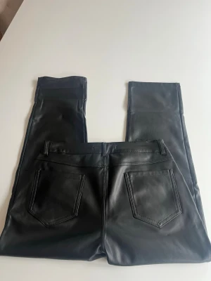 Svarta skinnbyxor  - Snygga svarta skinnbyxor med två bakfickor. Byxorna har en tight passform och ger en cool läderlook. Perfekta för dig som vill ha en edgy stil och gillar trendiga detaljer.