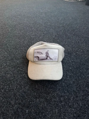 Två meshkepsar med retrotryck - Säljer två kepsar i meshmodell, en grå och en svart. Båda har unika retroinspirerade fototryck framtill – den grå med en person vid en bil och den svarta med ett gäng personer. Perfekt för dig som gillar streetwear och vintagevibbar.