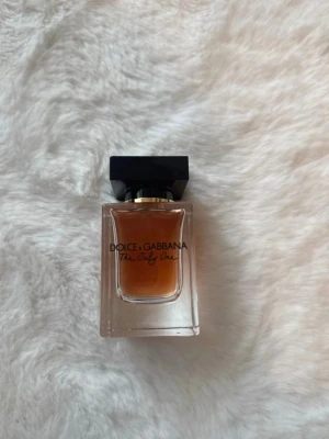 Dolce & Gabbana The Only One parfym - En lyxig parfym från Dolce & Gabbana, The Only One. Flaskan är rektangulär i genomskinligt glas med svart fyrkantigt lock och gulddetalj. Innehållet är bärnstensfärgat och flaskan har en elegant och modern design.